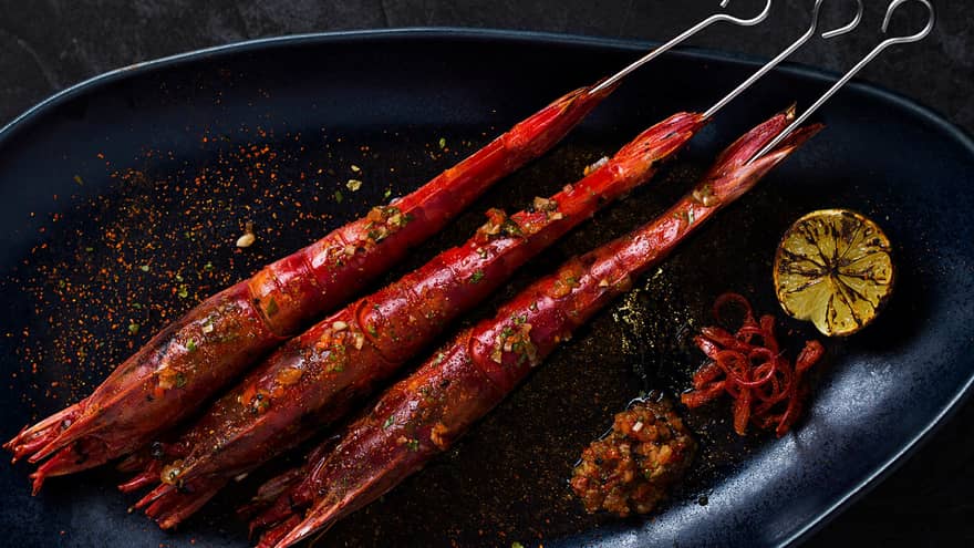 A close up of prana's on a skewer with lemons and dipping sauce on the side