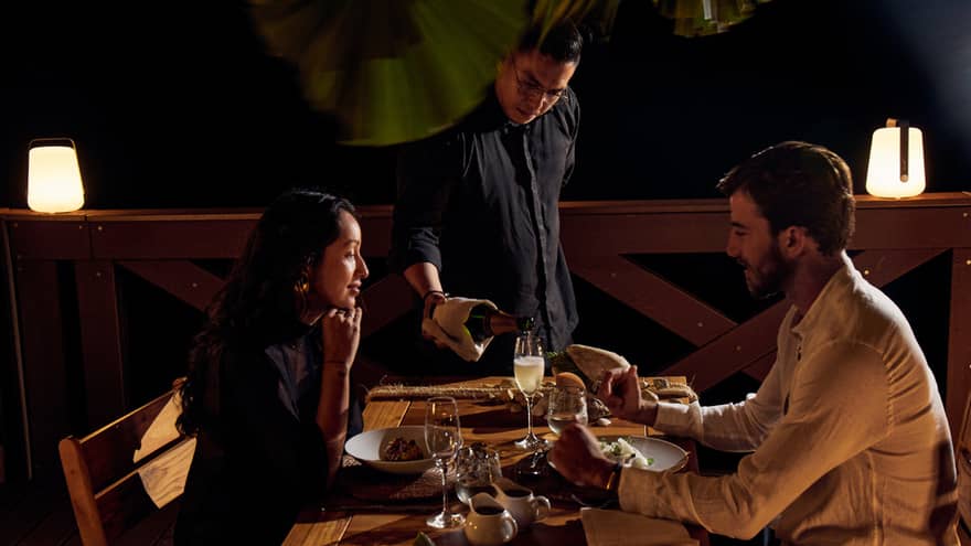 An elegant couple sharing an intimate dinner at a beautifully set table, while a graceful waiter pours champagne into their glasses
