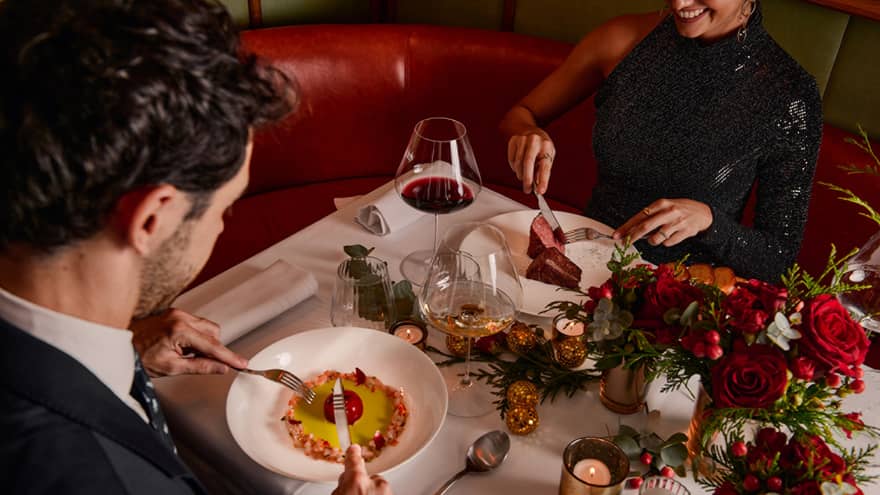 Two guests sitting at a dining table holding silverware to eat their food.