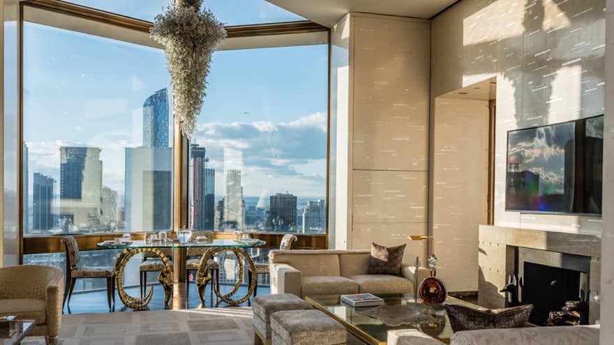 Bright Ty Warner Penthouse with modern gold dining table, chandelier by floor-to-ceiling window