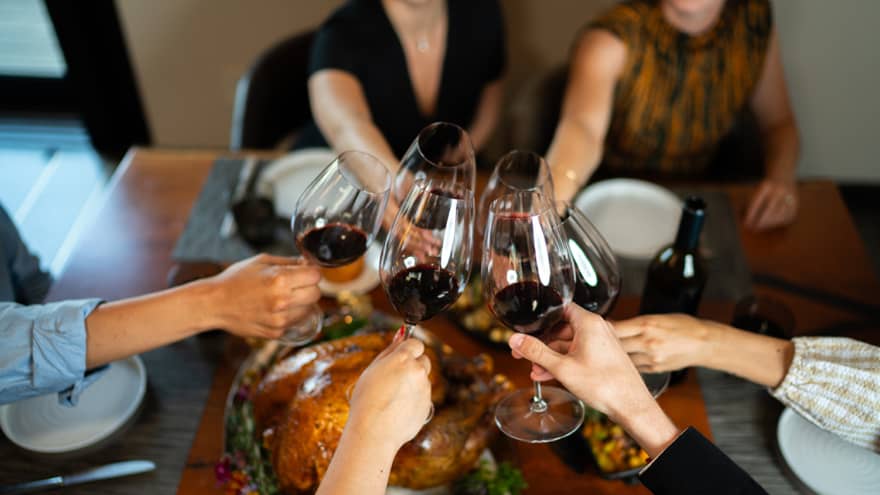 Six arms extend toward the middle of the table to toast over a meal, each holding a glass of red wine