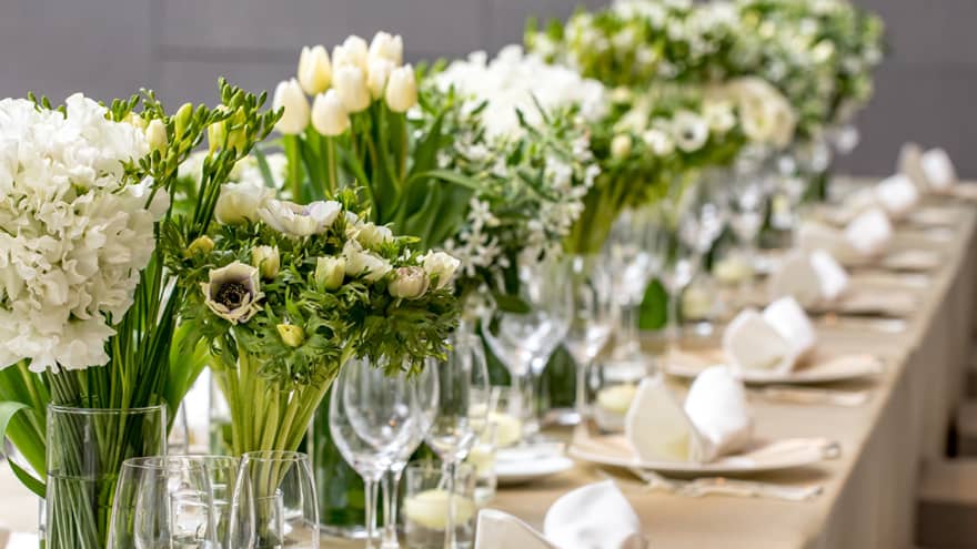 Close-up of long wedding dining table with wine glasses, white flowers in vases 