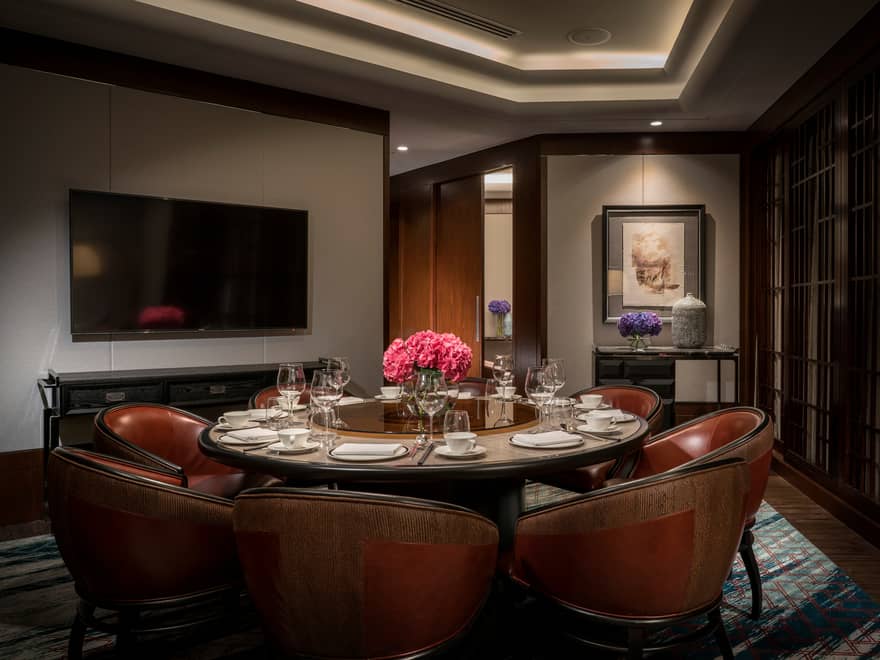 Dark red leather bucket seats around round dining table in business meeting room, TV on wall