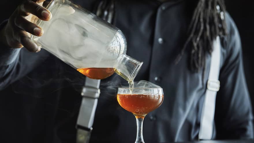 Smoke rolls off the decanter as a Four Seasons staff member pours bourbon into a coupe glass