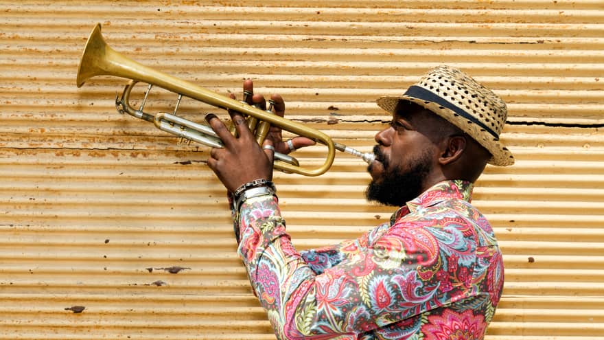 A man in a hat and colourful shirt playing a trumpet.