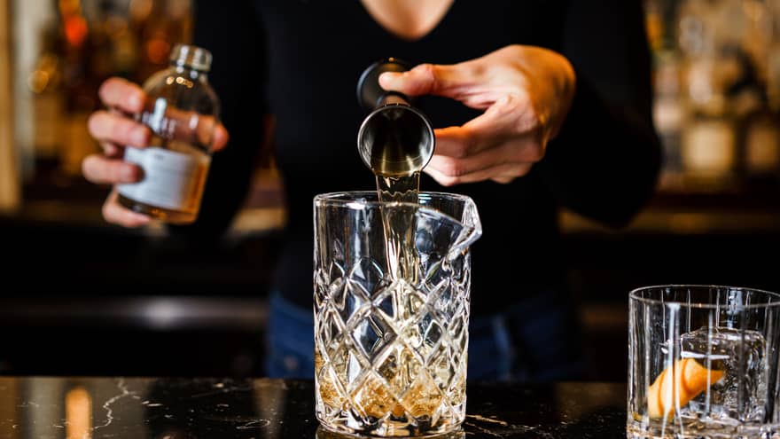 Person pouring a drink into a glass, with an empty glass beside it.