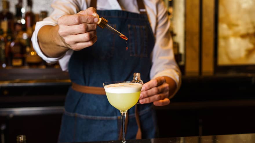 Bartender pouring a yellow coloured drink into a wine glass.