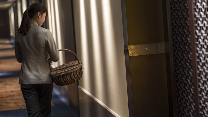 Hotel staff carries wicker basket down dimly-lit hall