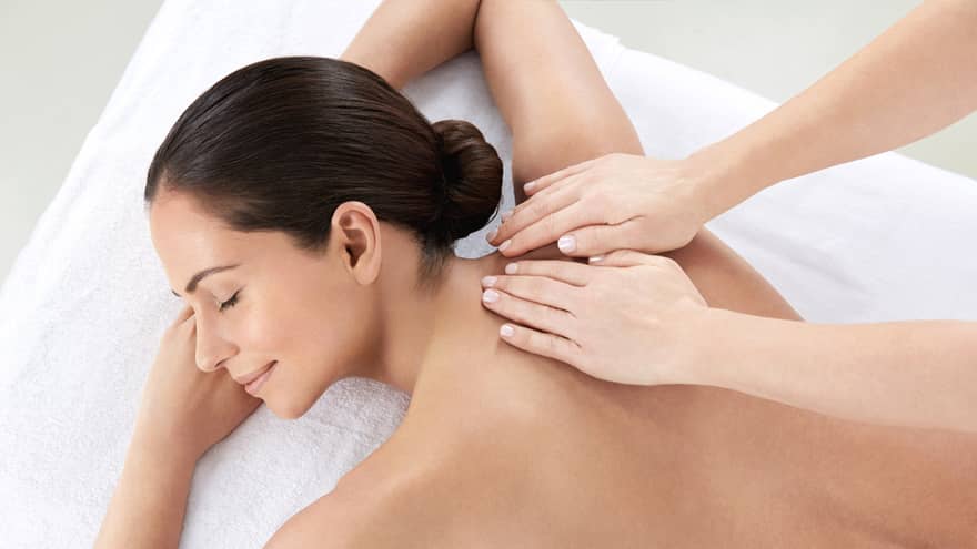 Woman smiles, lies on massage table as hands massage bare shoulders