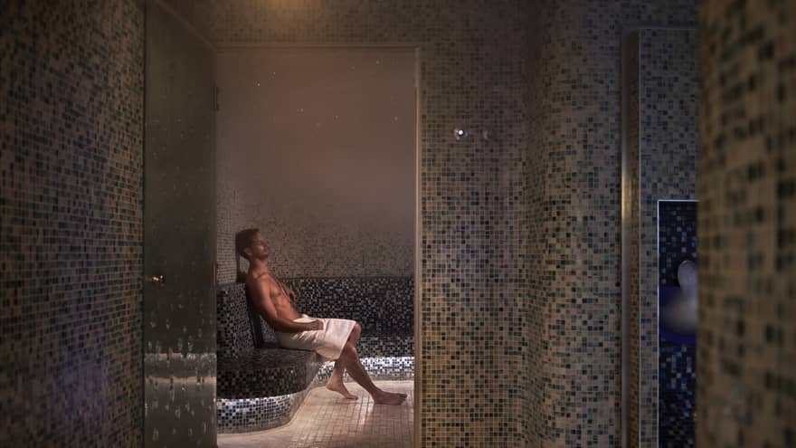 A man sitting with a towel in a dimly lit spa room.