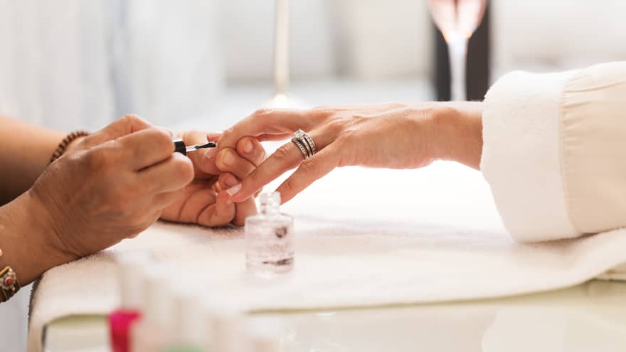 Close-up of woman in white robe getting clear polish manicure at spa table