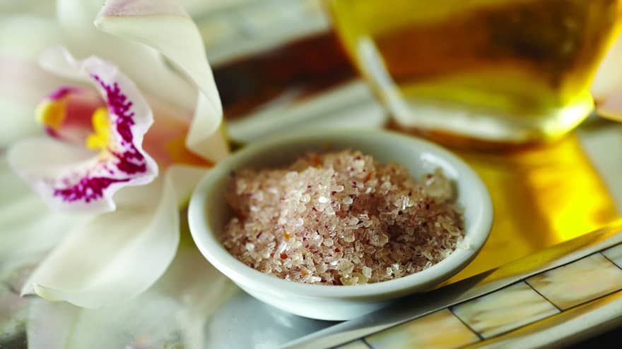 Small bowl with pink sea salt, beside tropical white-and-purple flower 