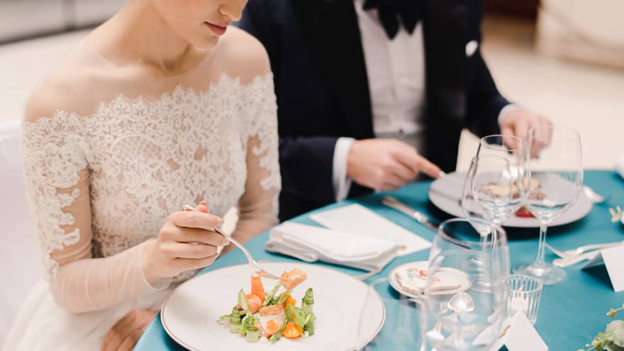 Bride and groom sitting at blue and white formally set table, eating salad