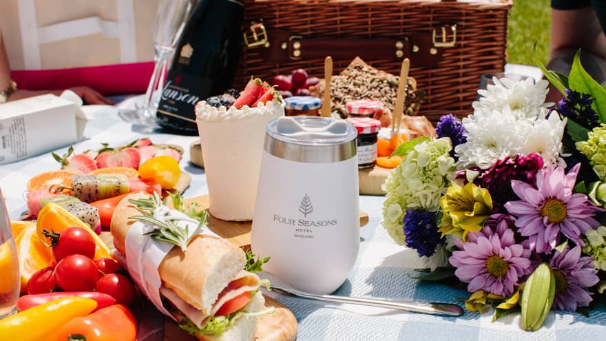A picnic blanket with a cup, flowers and fruit on it.