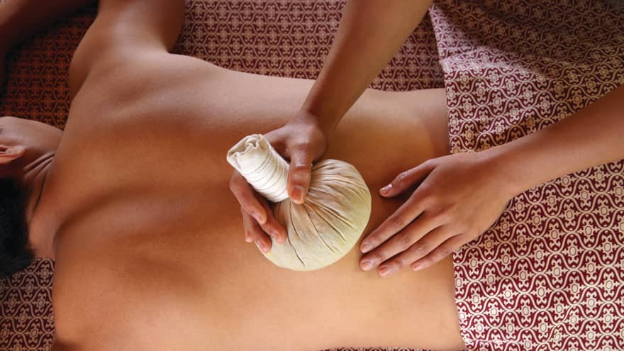 Masseuse rubs herbal sac on woman's bare back in spa