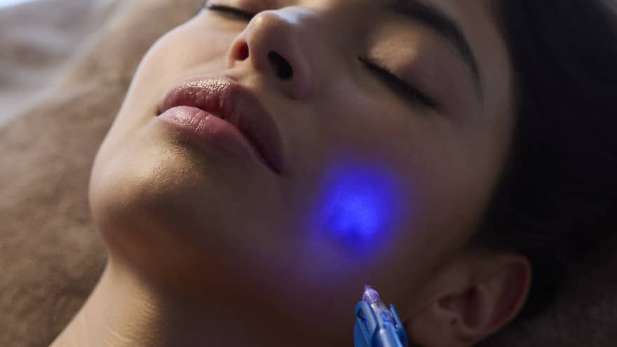 A person receives a facial treatment using blue light.