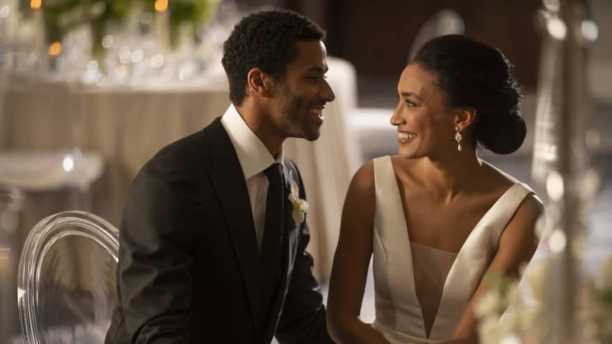 A couple in a suit and dress are sitting at a table smiling at each other.