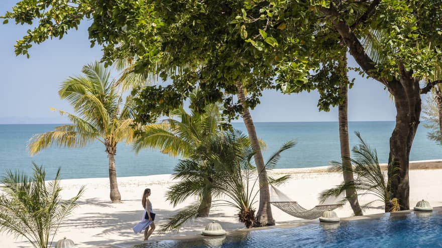 View of a woman walking on a tropical beach from a private pool