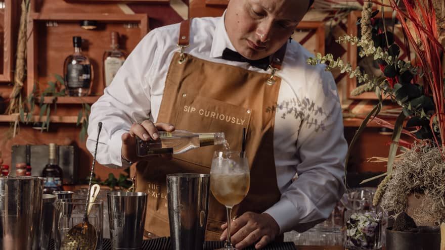 A bartender pouring a drink into a glass at the bar