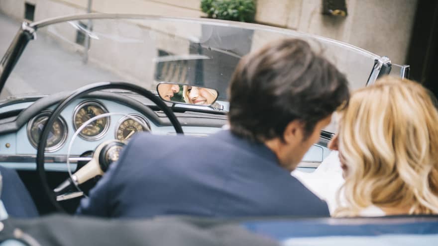 Couple sitting in front seats of classic convertible car lean in close