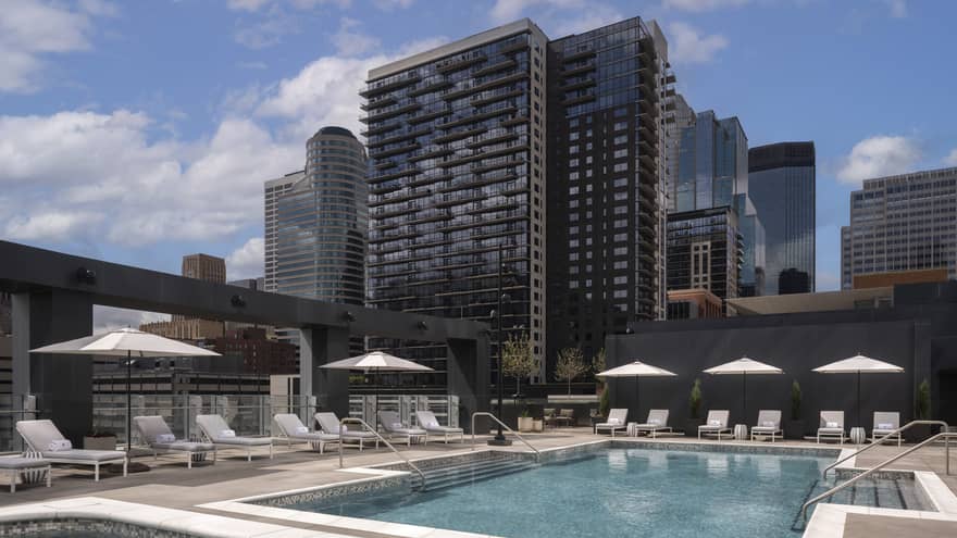 A pool with lounge chairs and umbrellas and city views in the background
