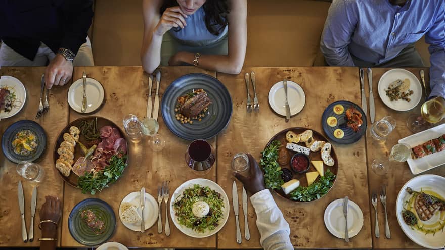 Aerial view of a group dining at a wooden table topped with various vibrant culinary dishes