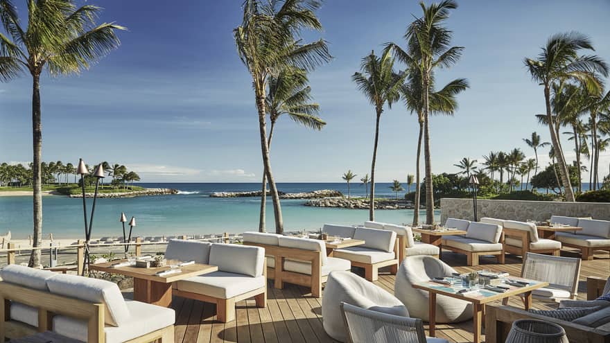 Plush white patio chairs around wood tables on sunny waterside Minas lounge