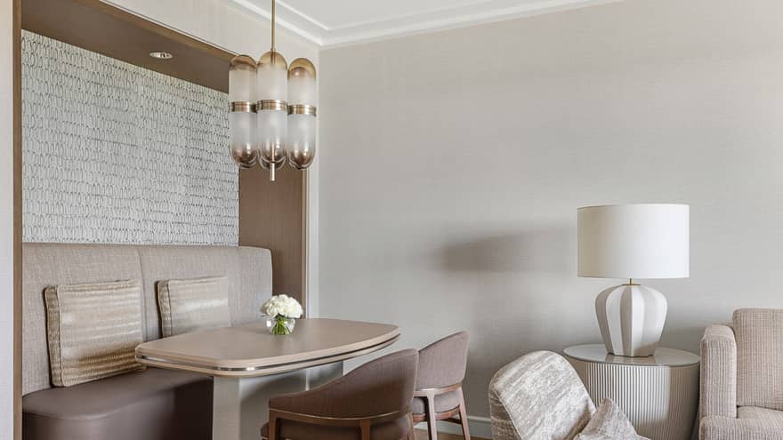 Dining table four four, with wall booth seating and two chairs, in a neutral-coloured living room