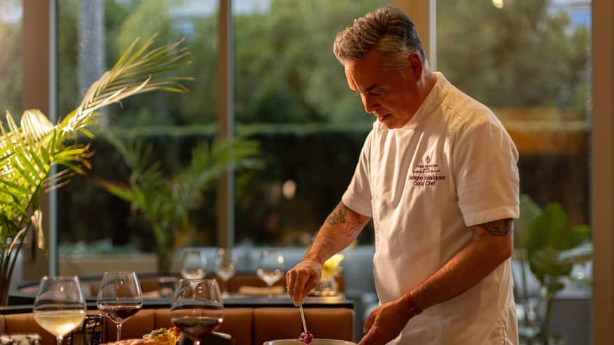 A chef standing at a dining table and preparing a meal