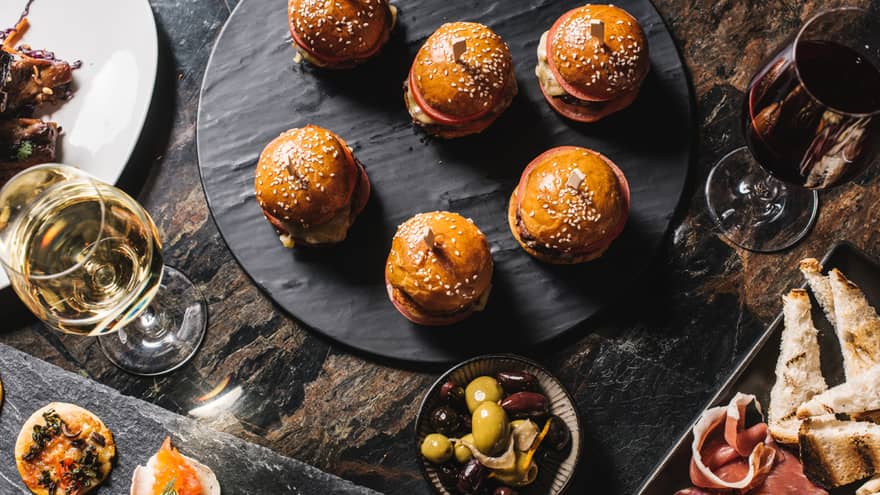 Aerial view of mini burgers, gourmet appetizers on slate stone trays, glass of white wine