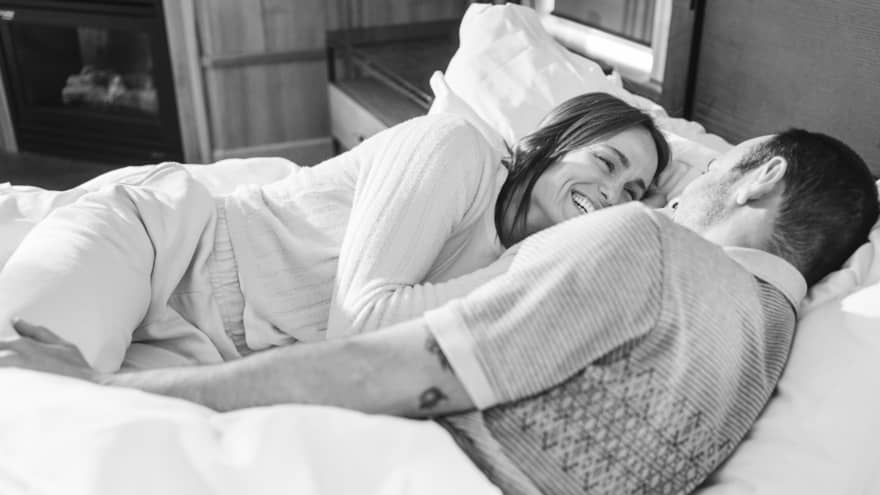Laughing couple lies together in bed