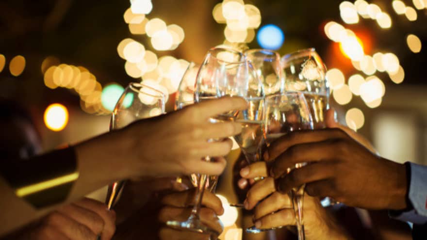 A group of guests clink their glasses of champagne together on a patio with twinkle lights