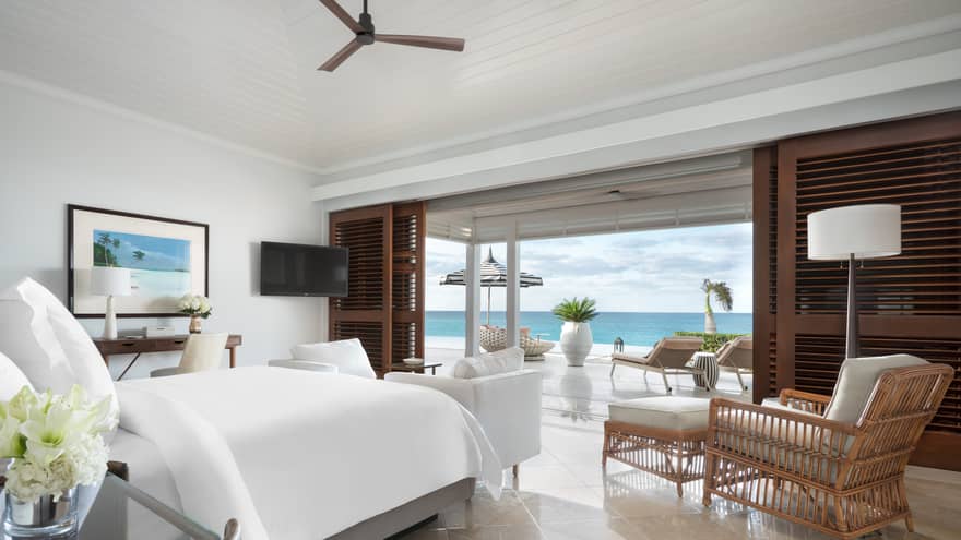 Beachfront villa residence bedroom with a bed, cozy seating area and a private terrace with loungers overlooking the ocean