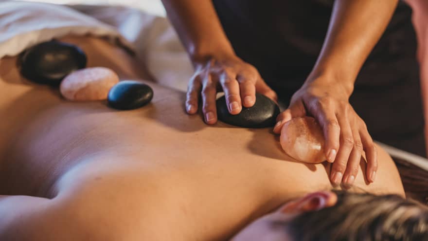 Close up of hands massaging warm stones on a woman's bare back