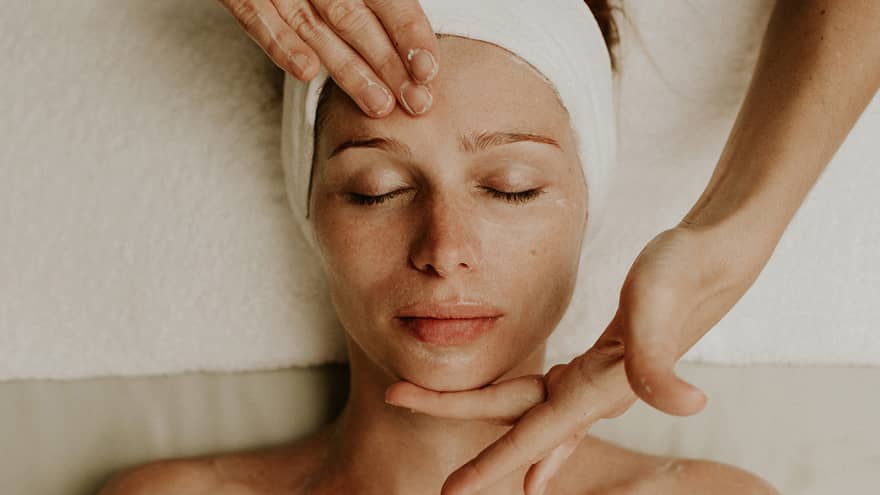 Person receiving a relaxing facial massage with eyes closed and head wrapped in a towel