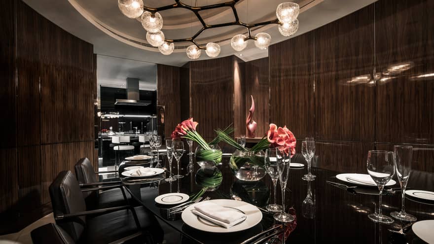 Penthouse private dining table with 12 seats under modern chandelier and vases with red flowers