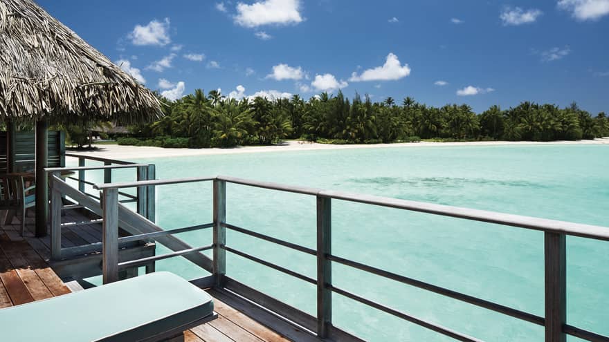 Overwater bungalow deck railings looking out at shallow blue lagoon and white sand beach