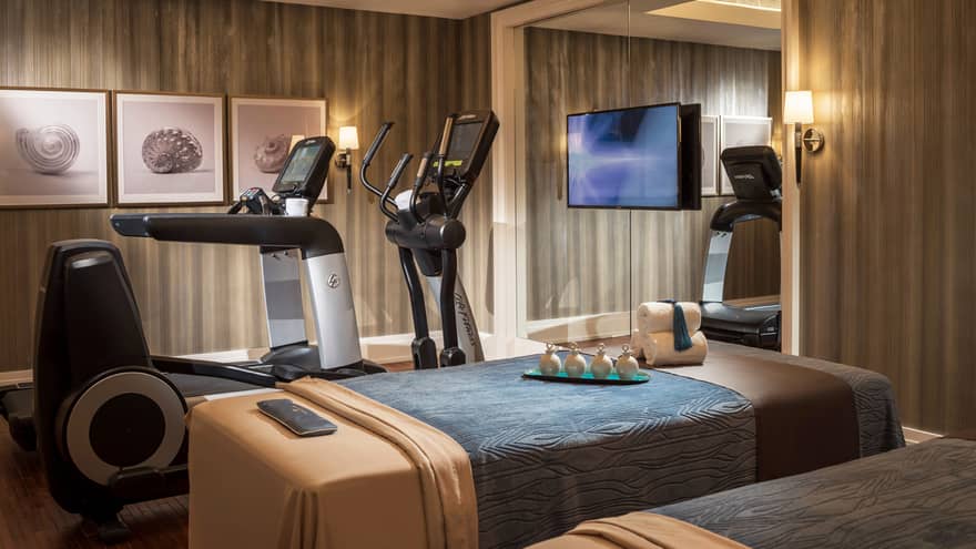 Private room with two massage tables beside two cardio machines, in front of mirror