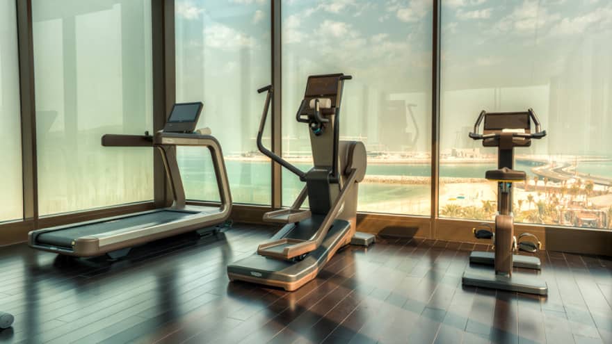 A treadmill, elliptical machine and cardio bike side-by-side at window overlooking beach