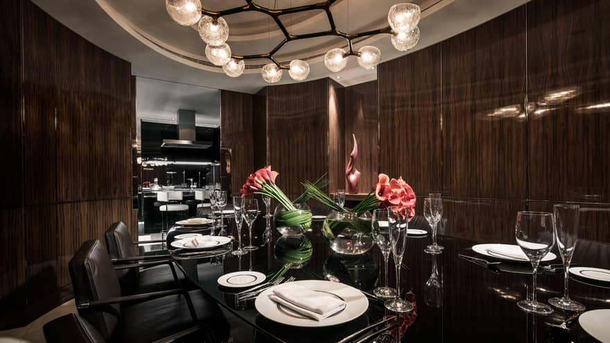 Penthouse private dining table with 12 seats under modern chandelier and vases with red flowers