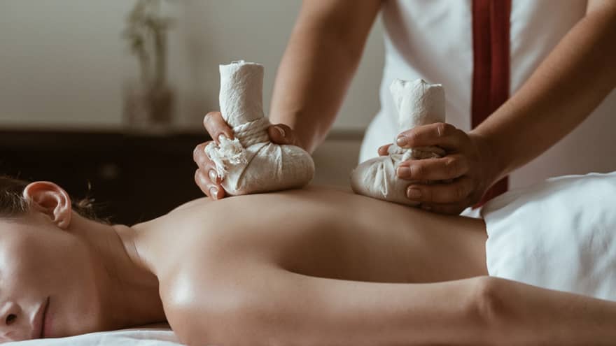 A woman being massaged by heavy stones in cloth bags.