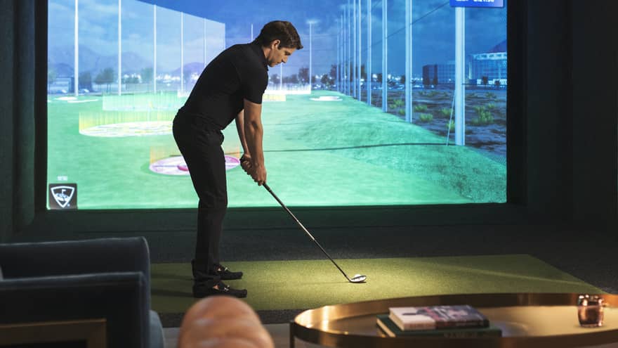 Man with golf club stands in front of screen showing Virtual Fairway