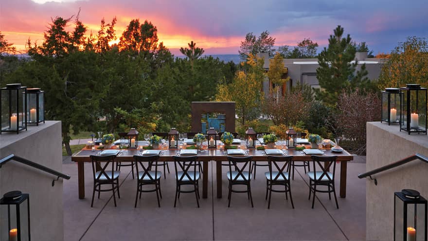 Long, elegant black dining table with black chairs, lanterns and flowers on outdoor terrace at dusk