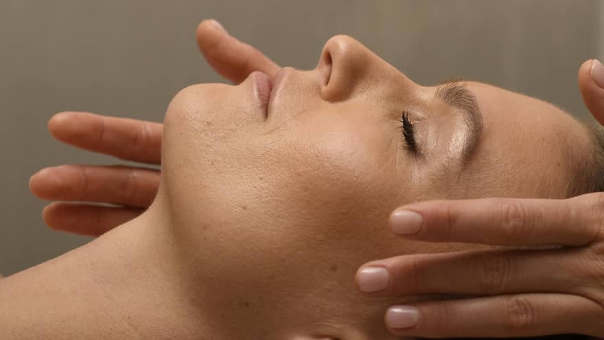 Person?s head lying on spa table with a person?s hands on the sides of the head