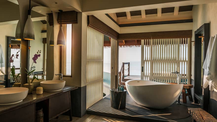 Water Villa bathroom, large freestanding white tub by sliding wood shutters, window, double sinks