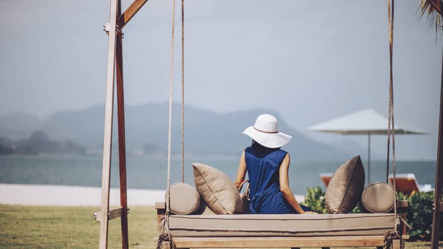 Woman in blue dress and white sun hat lounges on outdoor swing