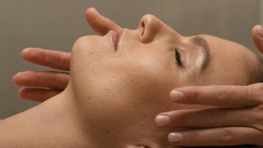 Person?s head lying on spa table with a person?s hands on the sides of the head