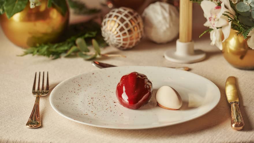 Modern, glossy, red ice cream dessert on a plate, with festive ornaments as decoration on the table