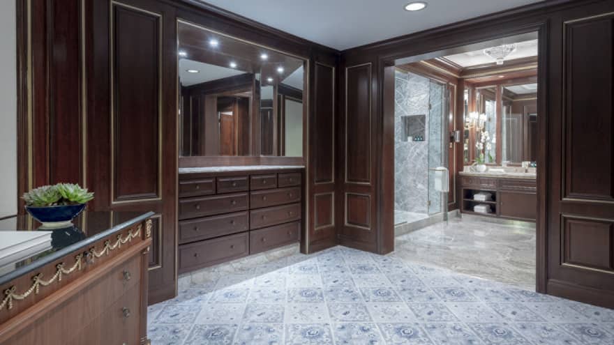 Dark wooden built-in closet shelving on a grand hotel suite, with double doors opening to bathroom