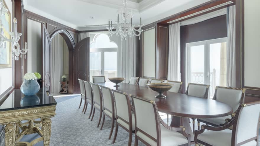 Elegant dining room with 14 seats, long wooden table, natural light, chandelier, ornate golden side table